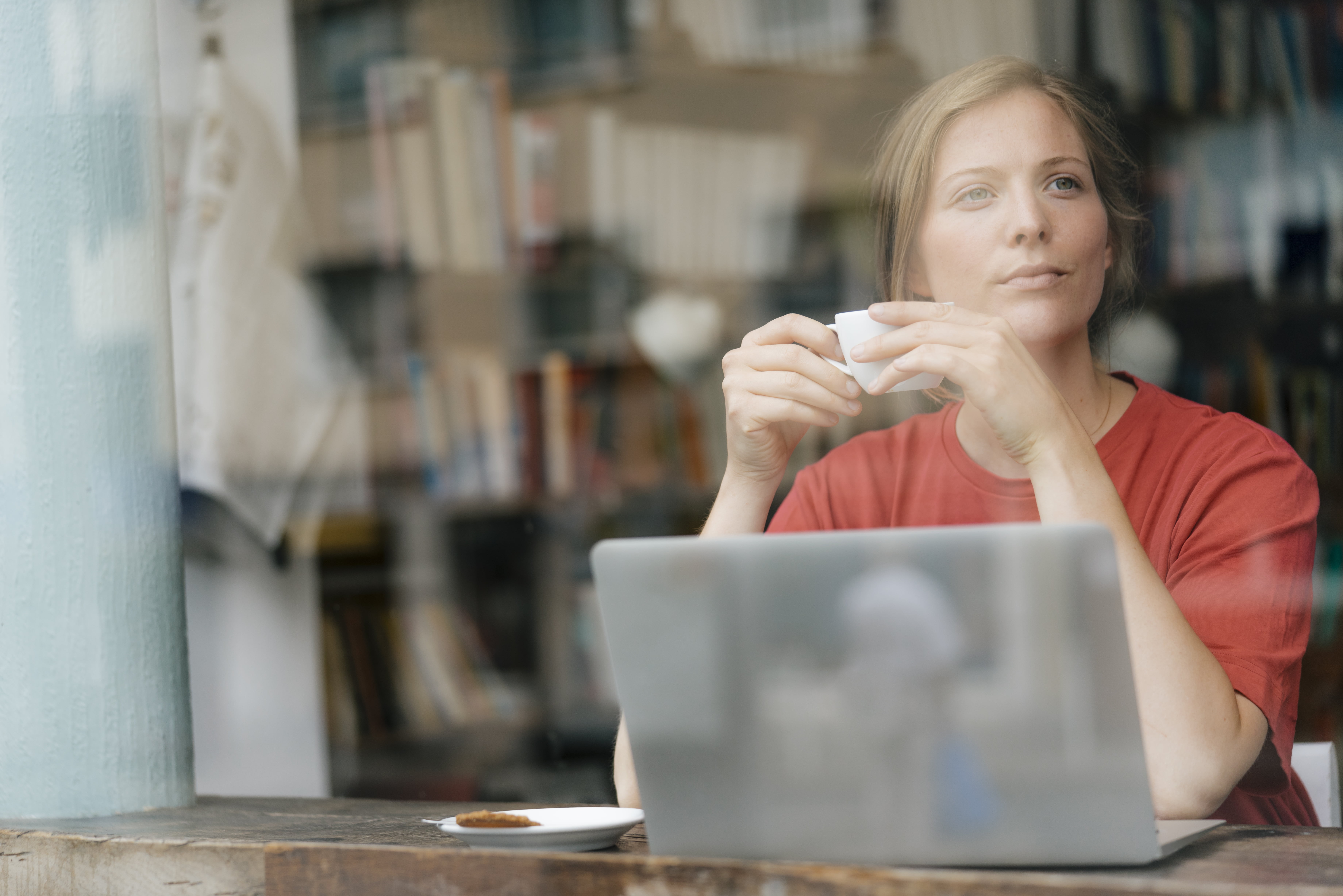 Dame som sitter foran PC med en kaffekopp i hendene