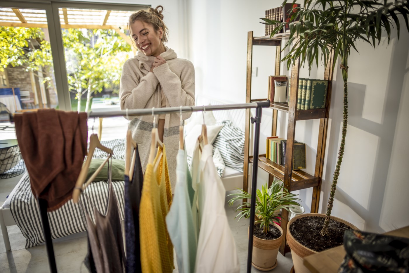 Kvinne smiler og holder en genser foran et klesstativ i stua. Hun rydder i klærne og får bedre oversikt i hverdagen.