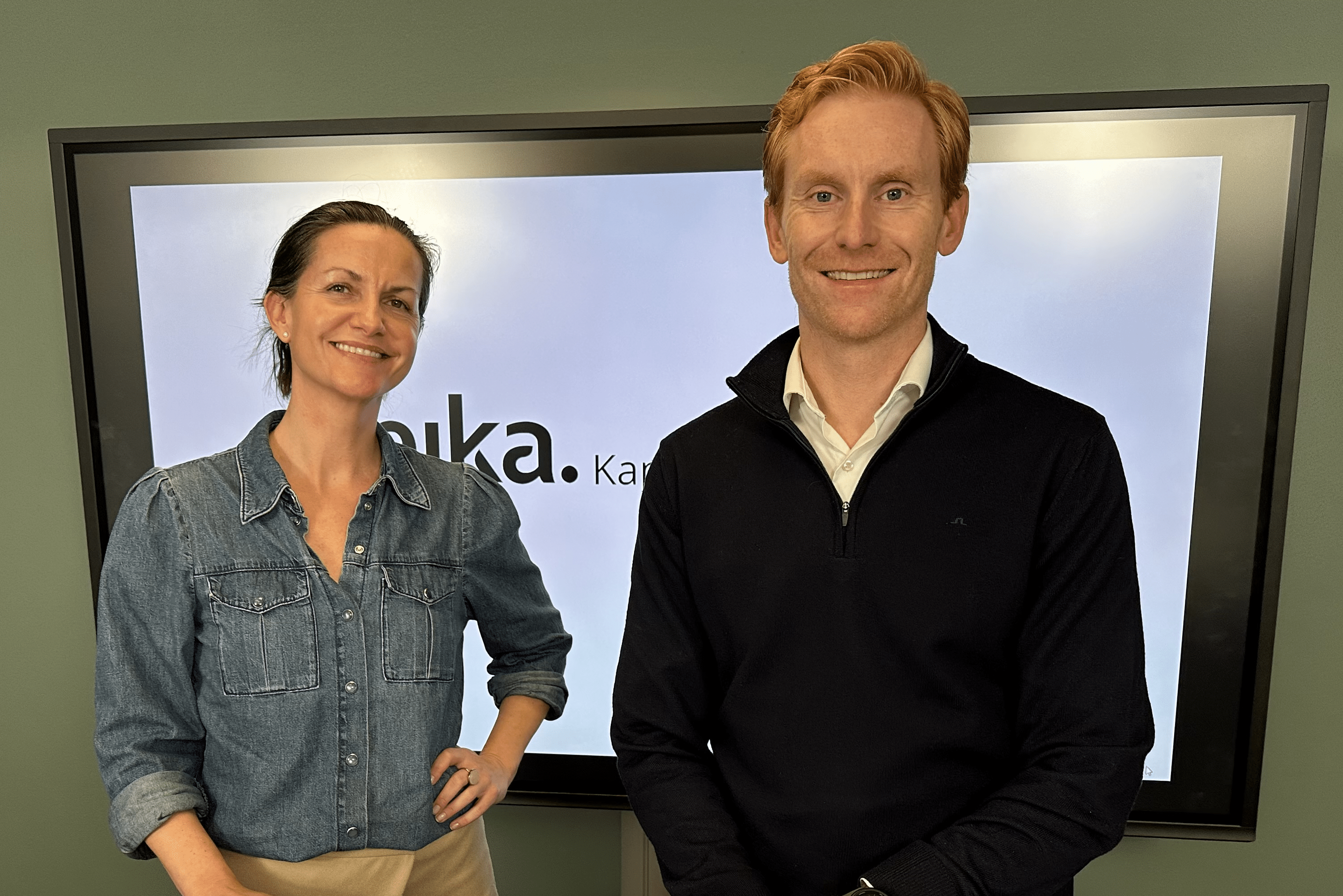 En blid Stine og Magnus står i et kontor i Eika
