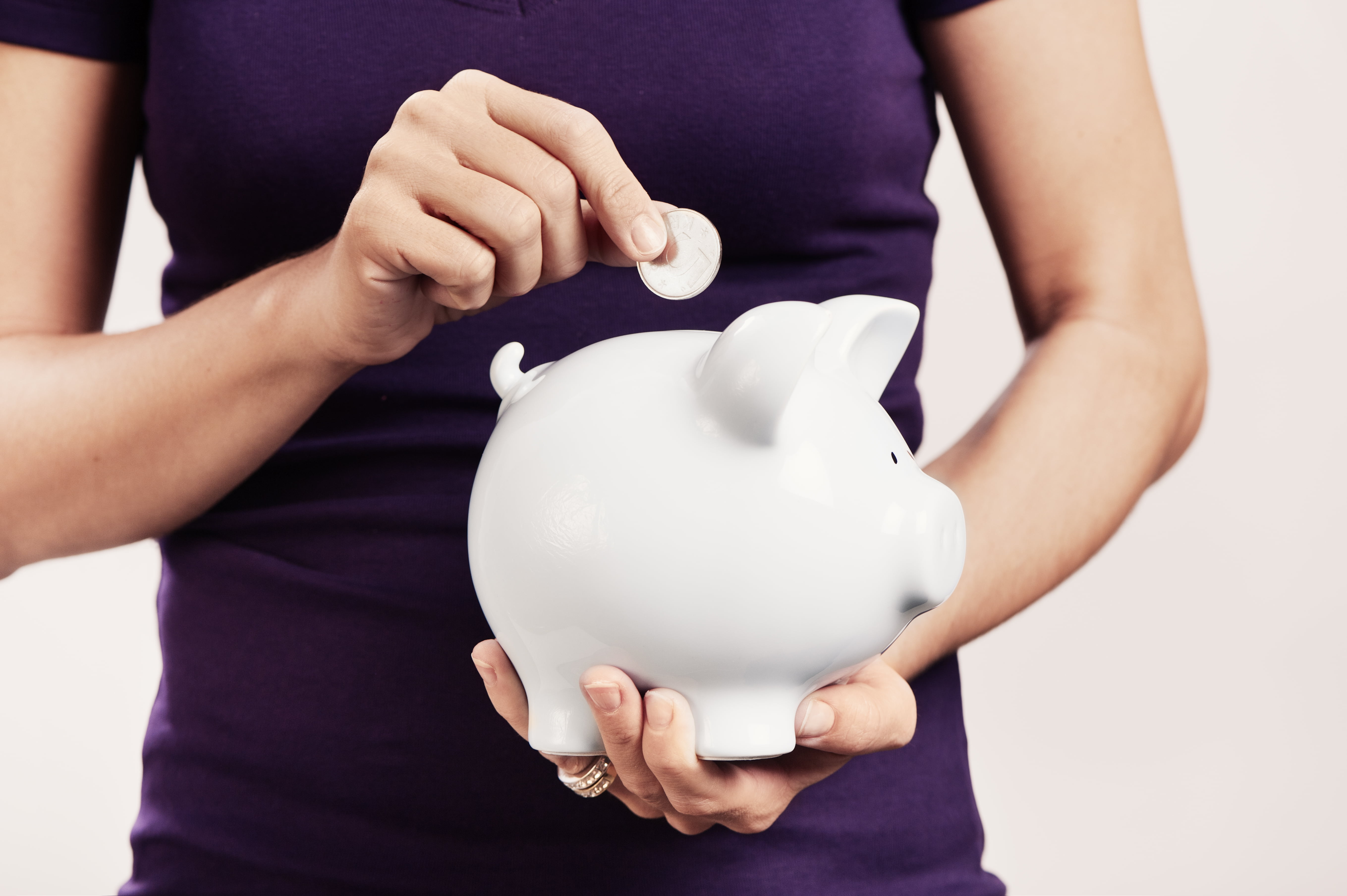 en person med lilla t-skjorte holder en mynt over en hvit sparegris